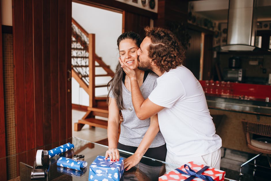 A joyful couple shares a kiss with wrapped gifts in a cozy indoor setting.