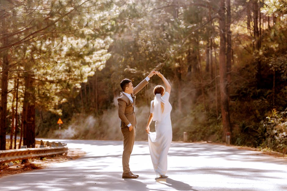 A bride and groom dance on a sunlit forest road, celebrating love and togetherness.