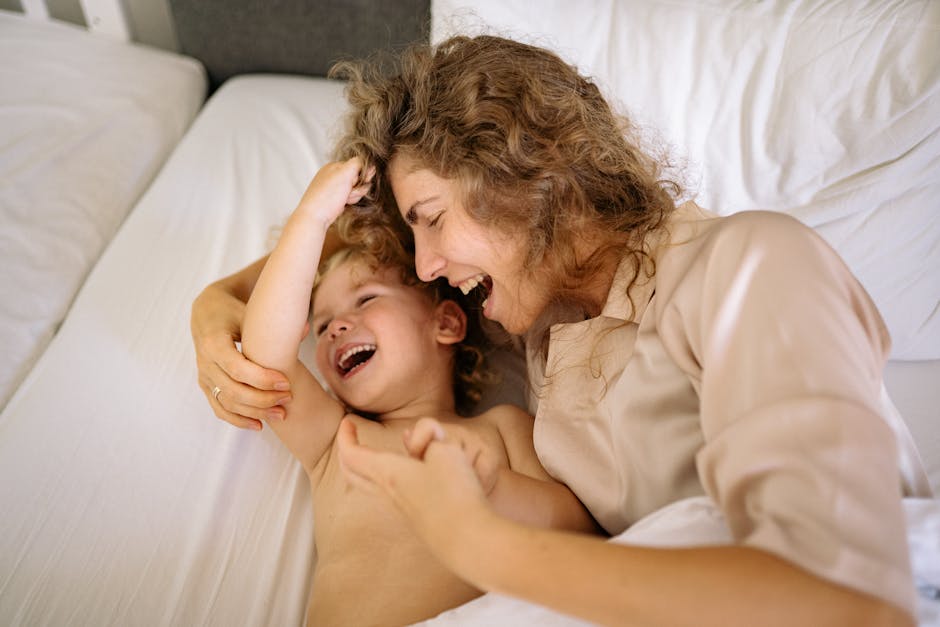 Mother and son laughing and bonding in a cozy bedroom setting, enjoying a playful moment together.
