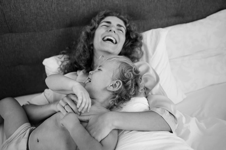 A heartwarming black and white image of a laughing mother and child bonding on a bed.