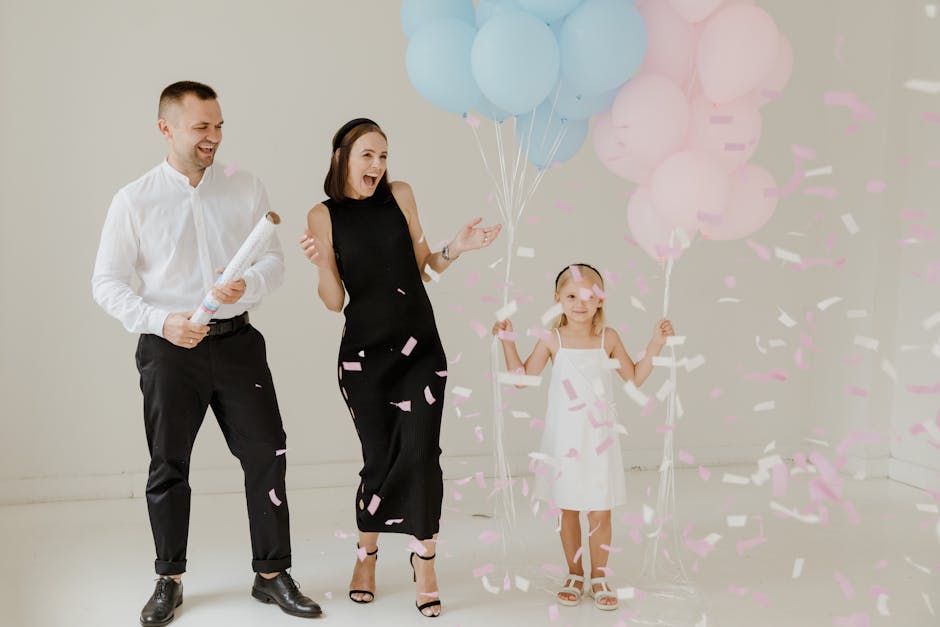 Happy family celebrating a gender reveal with blue and pink balloons and confetti indoors.