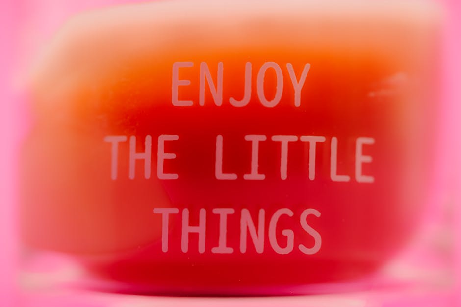 Close-up of 'Enjoy the little things' text on a pink gradient background, inspiring positivity.