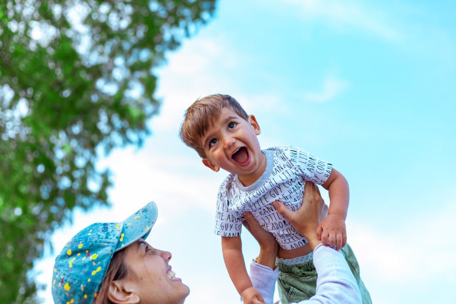 A mother lifts her happy child against a clear blue sky, capturing a moment of joy and togetherness.
