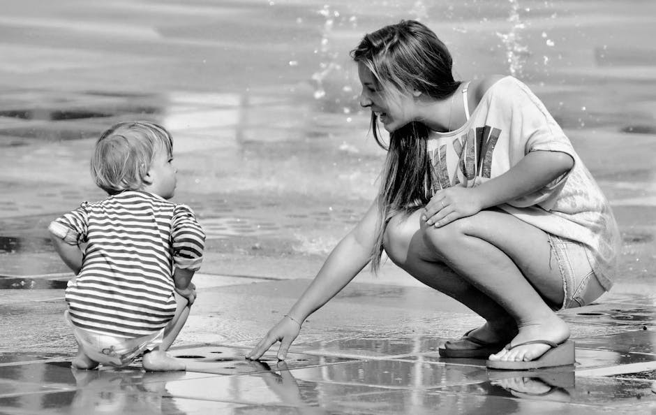 A monochrome capture of a woman and child enjoying playful moments by a fountain.