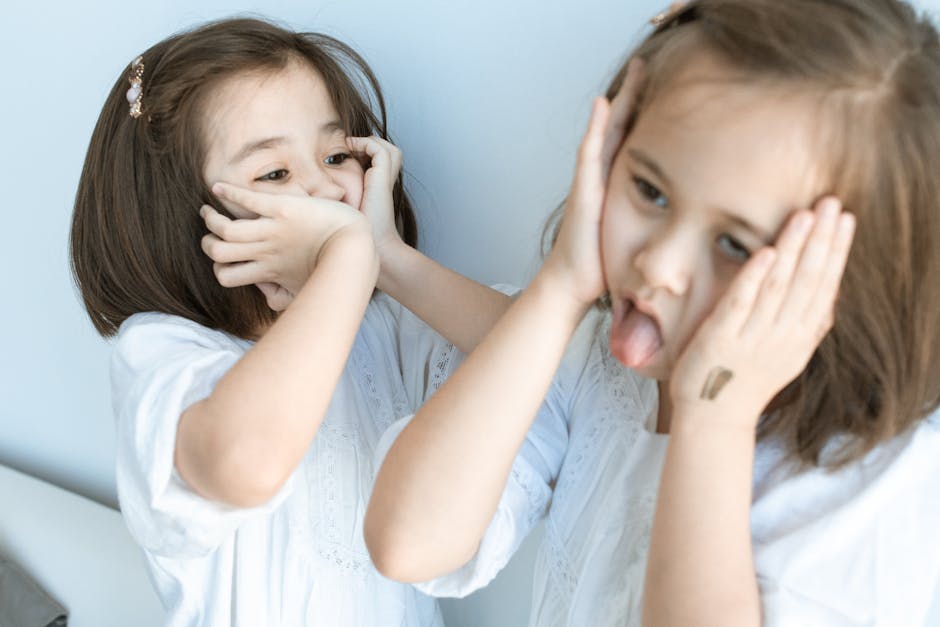 A young Asian girl playfully making faces at her reflection in the mirror, enjoying a light-hearted moment indoors.