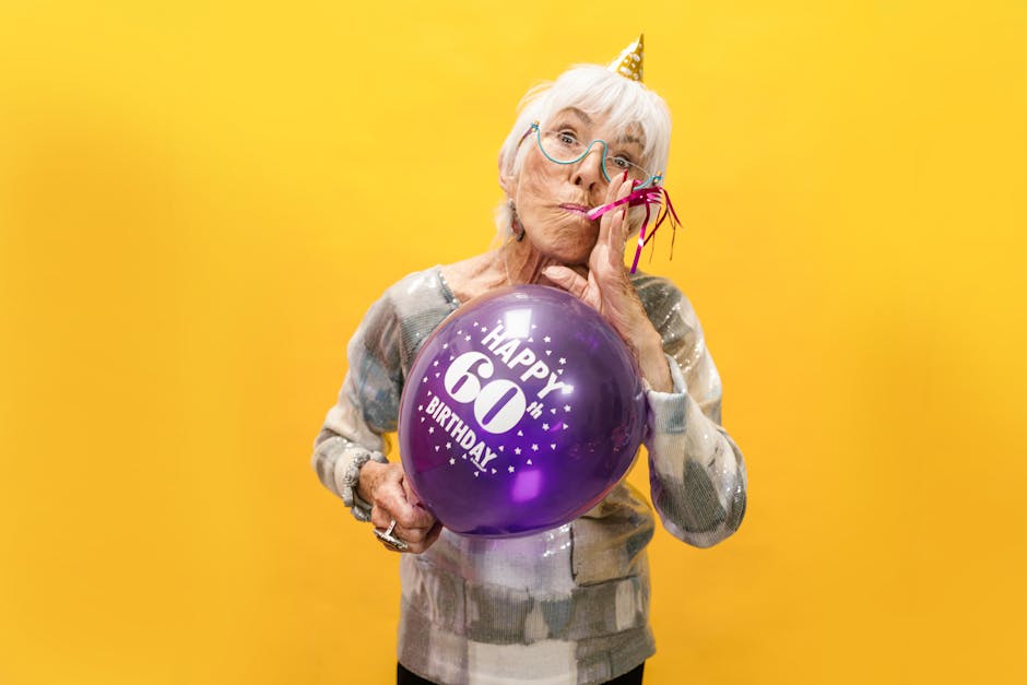Elderly woman celebrating her 60th birthday with a vibrant balloon against a yellow background.
