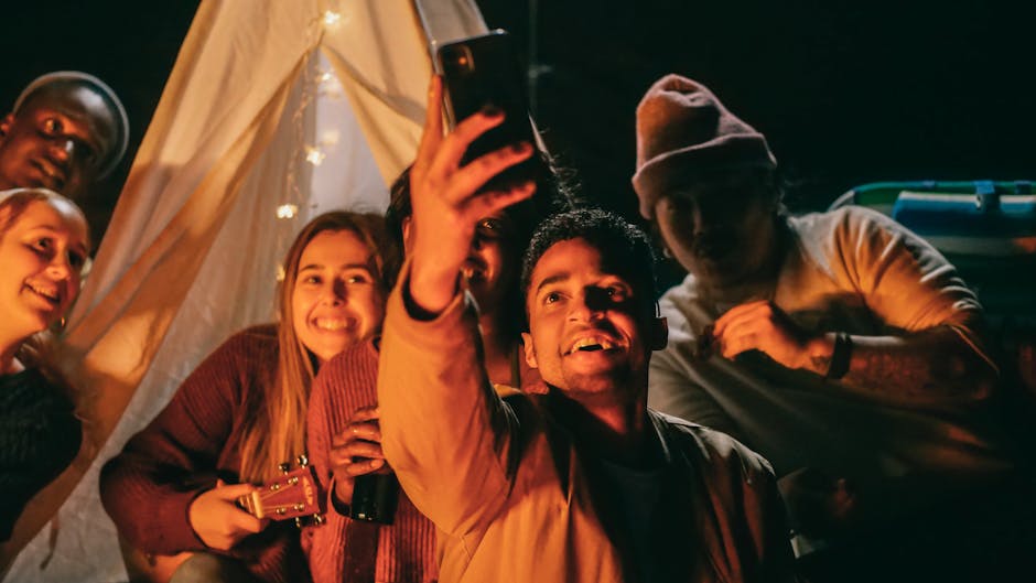 A joyful group of friends takes a selfie together at a nighttime camping gathering.