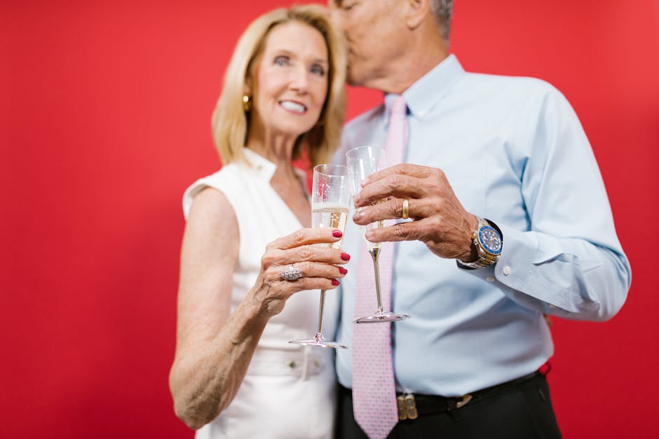 Senior couple celebrating an anniversary with champagne against a red backdrop, embodying elegance and love.