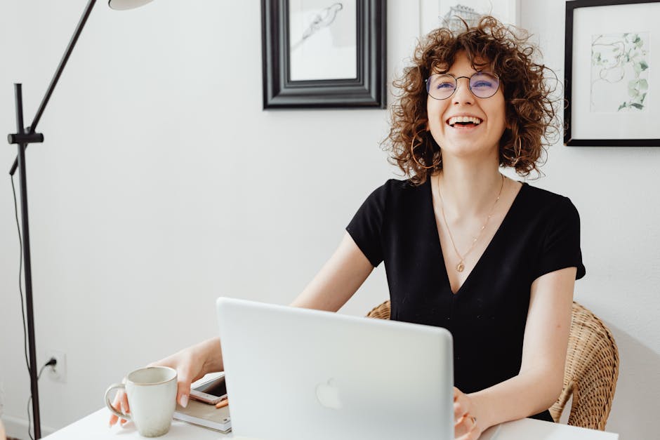 Smiling woman with curly hair using a laptop at a bright home office desk.
