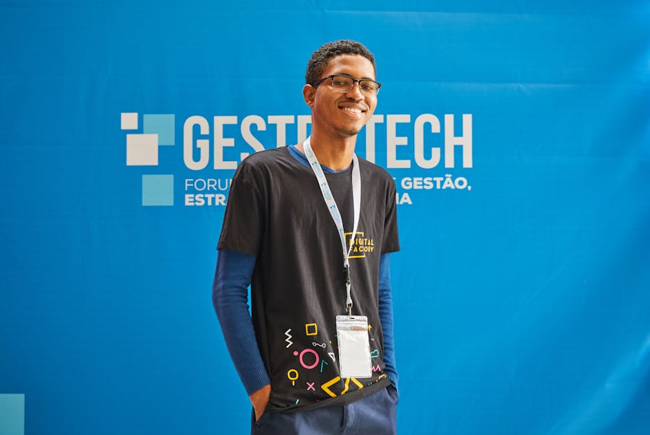 Young man posing at a business conference with a blue background, smiling confidently.
