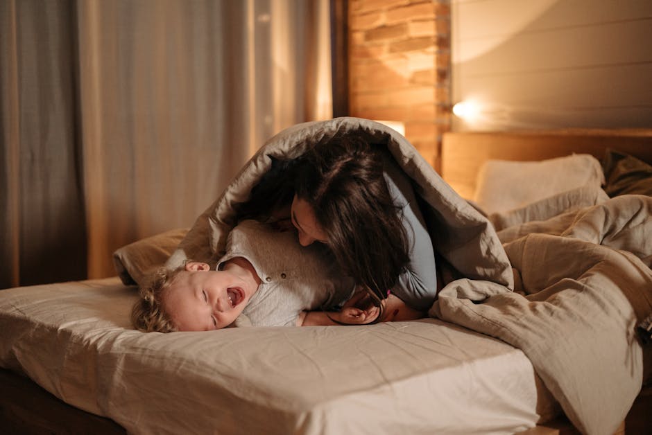 Mother and child joyfully playing under a comforter in a cozy bedroom setting.