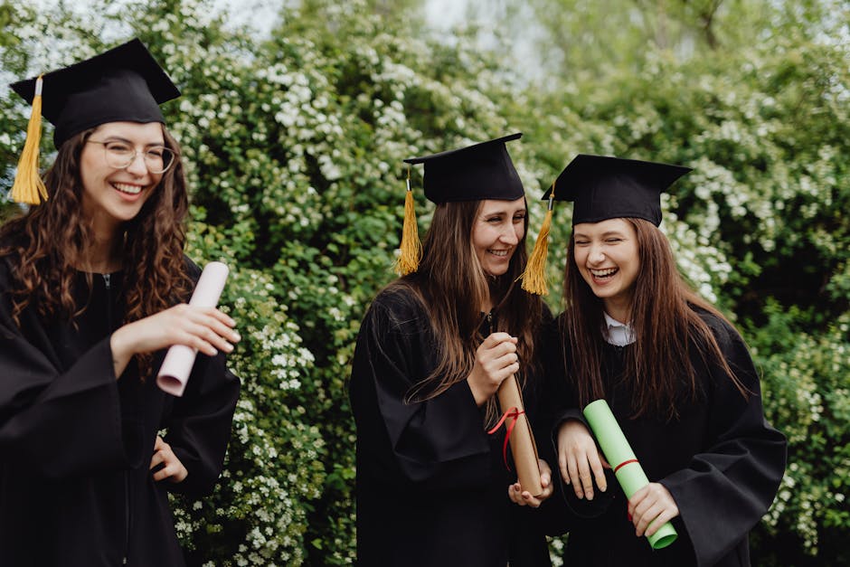 Group of happy female graduates in caps and gowns laughing and holding diplomas outdoors.