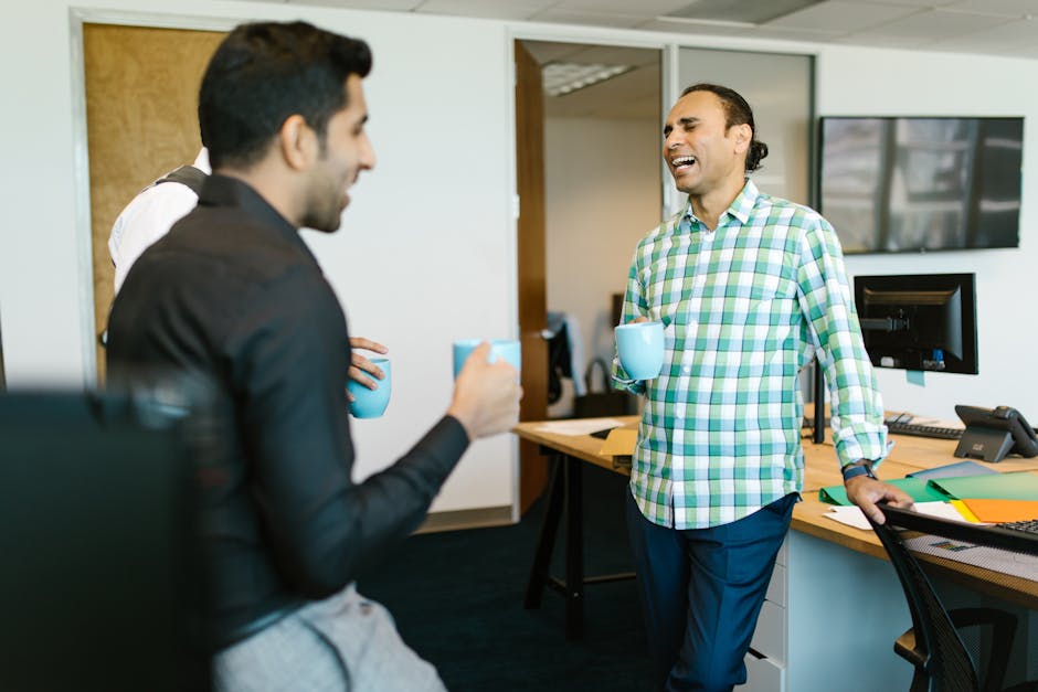 A group of coworkers laughing and enjoying a coffee break in a modern office setting.