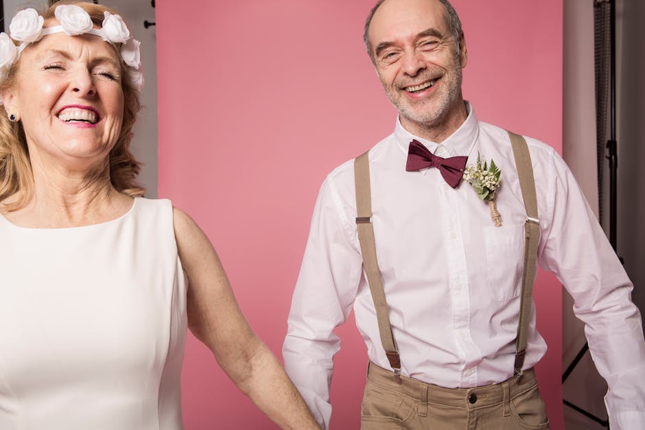 Cheerful elderly couple smiling and holding hands in a pink studio, exuding love and togetherness.