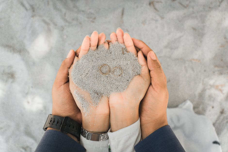 Close-up of a couple holding wedding rings in sand, symbolizing love and union.