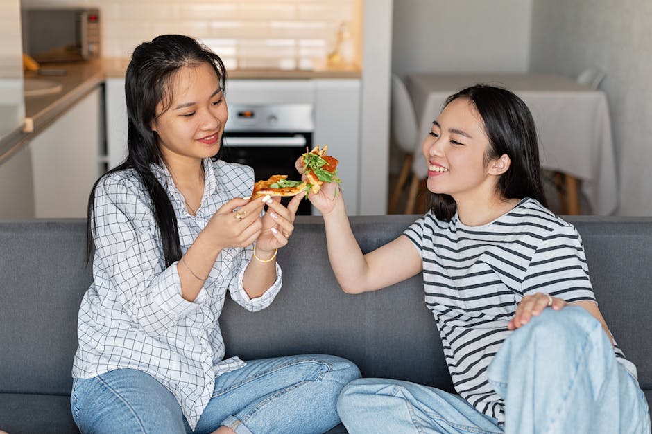 Smiling friends sitting on a sofa, sharing delicious pizza in a cozy indoor setting.