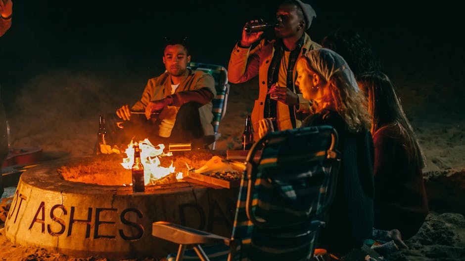 A group of friends enjoying drinks by a bonfire on the beach at night, capturing a warm and social atmosphere.
