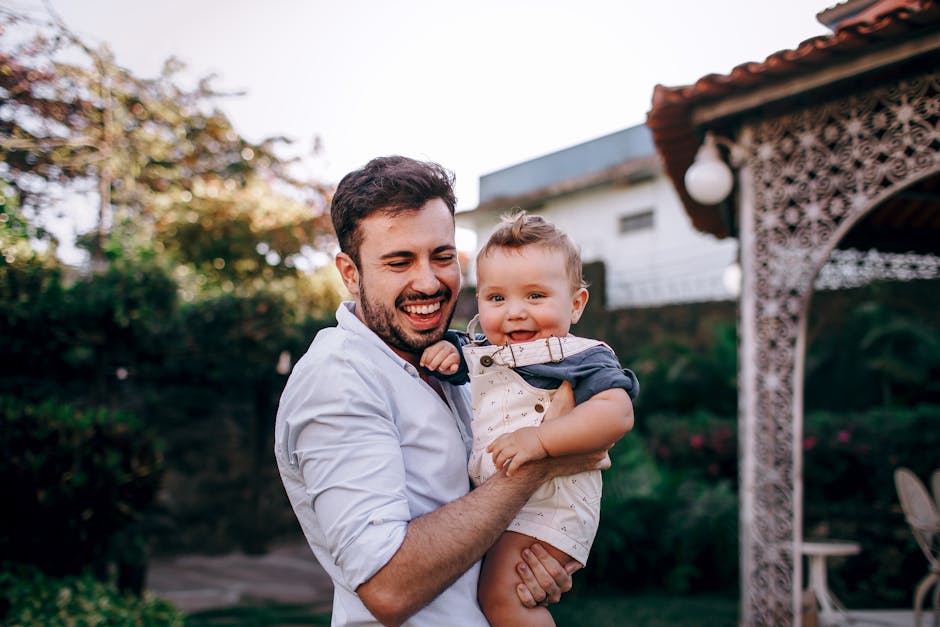 A joyful father holding his smiling baby son in an outdoor setting.