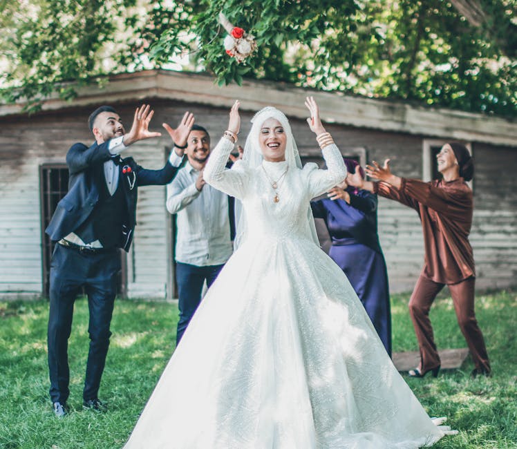 A happy bride tosses her bouquet at a vibrant outdoor wedding celebration.