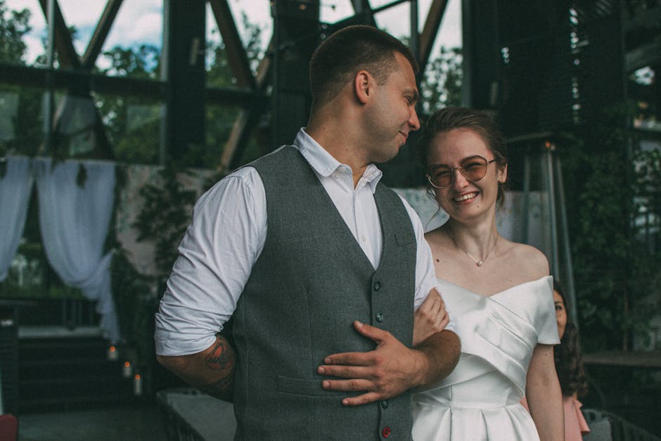 A joyful couple in wedding attire smiling at each other in an outdoor setting.