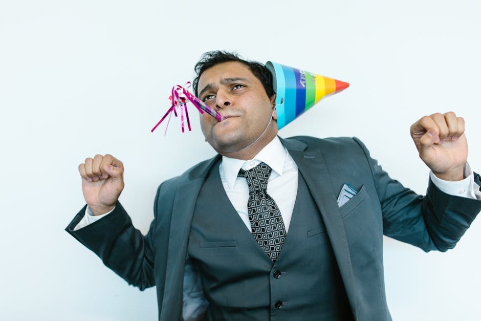 A joyful businessman wearing a suit and party hat, celebrating indoors.
