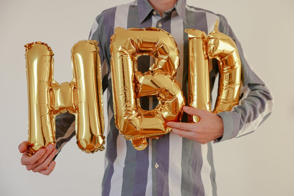 Adult holding golden balloon letters 'HBD' for a birthday celebration indoors.