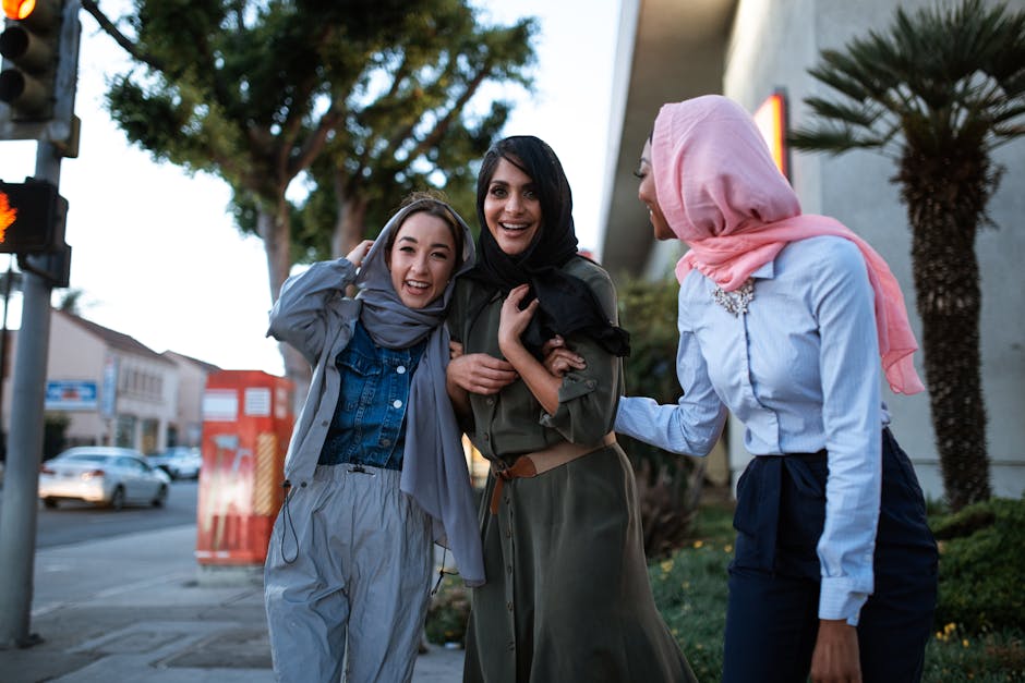 Three diverse women in hijabs smiling and enjoying each other's company outdoors, showcasing cultural diversity and friendship.
