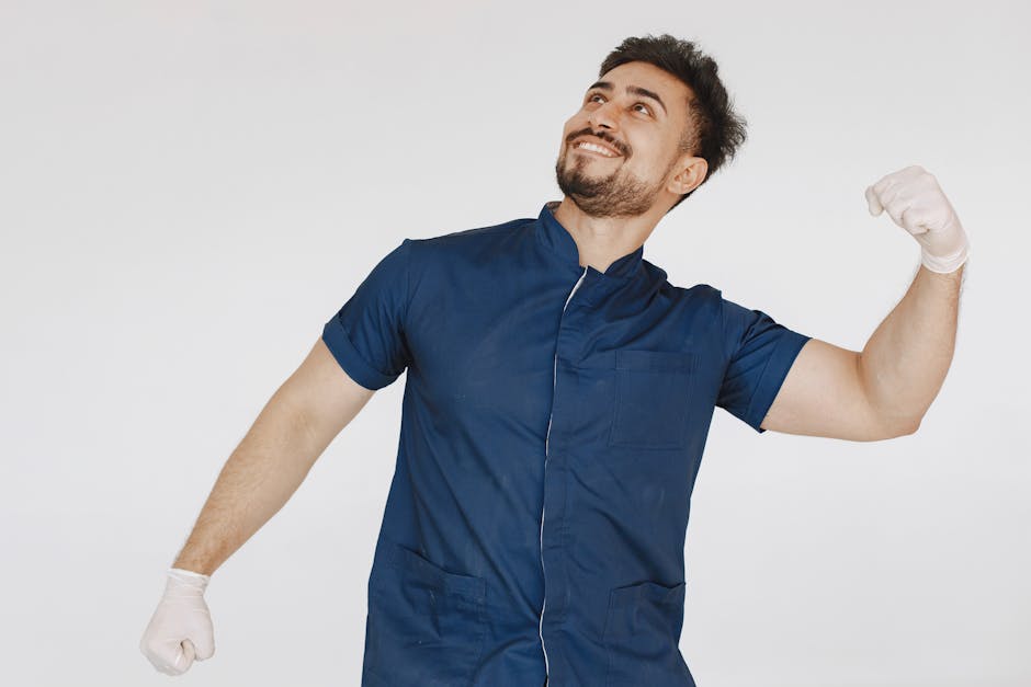 Smiling male medical professional in blue scrub suit poses confidently against a plain white background.