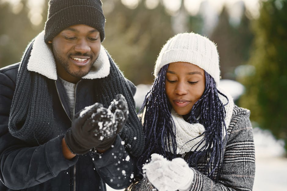 Smiling couple playing with snow outdoors in winter wearing cozy clothing.