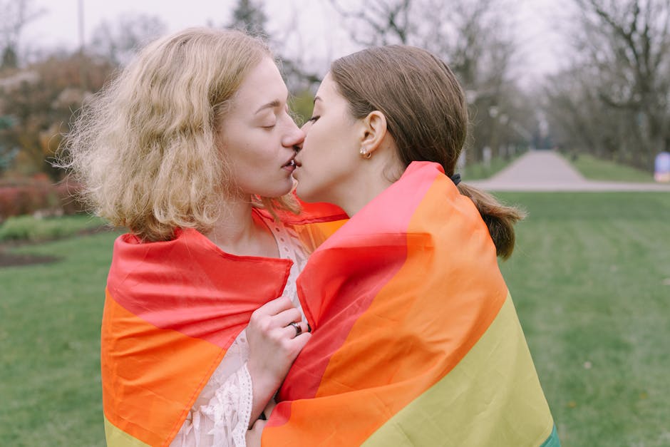 Two women sharing a romantic kiss wrapped in a rainbow flag, symbolizing love and pride.