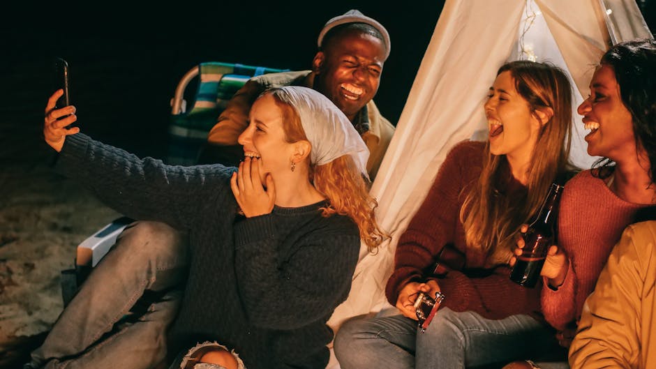A joyful group of friends capturing memories at a beachside campfire gathering.