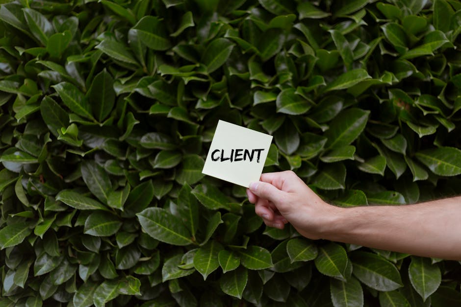 Close-up of a hand holding a note with the word 'CLIENT' in front of a lush green leafy background.
