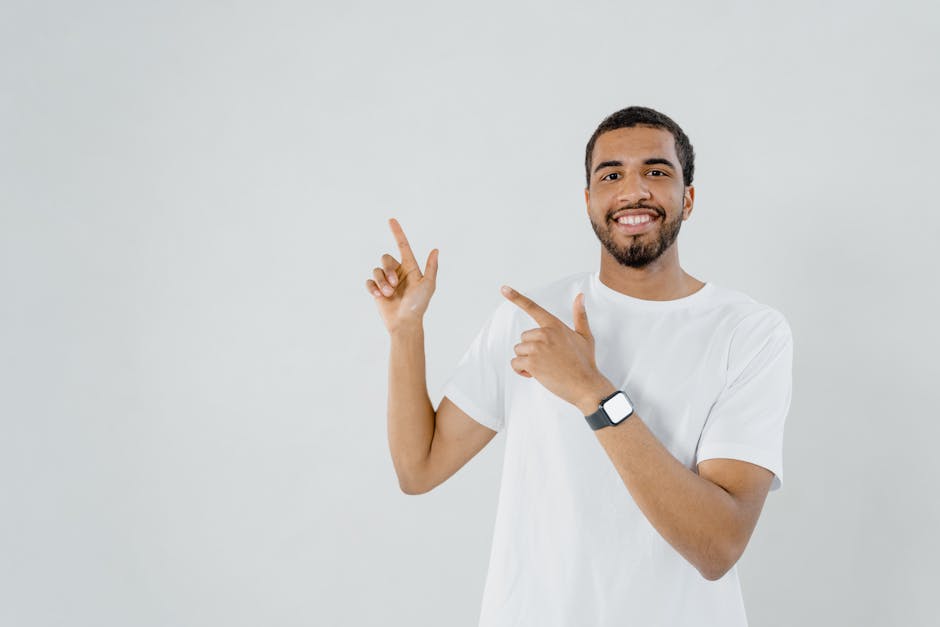 Smiling man in a white shirt pointing at blank copy space in a studio setting.