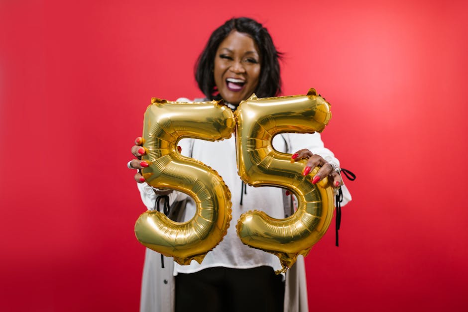 Smiling woman celebrating her 55th birthday with gold balloons against a red background.