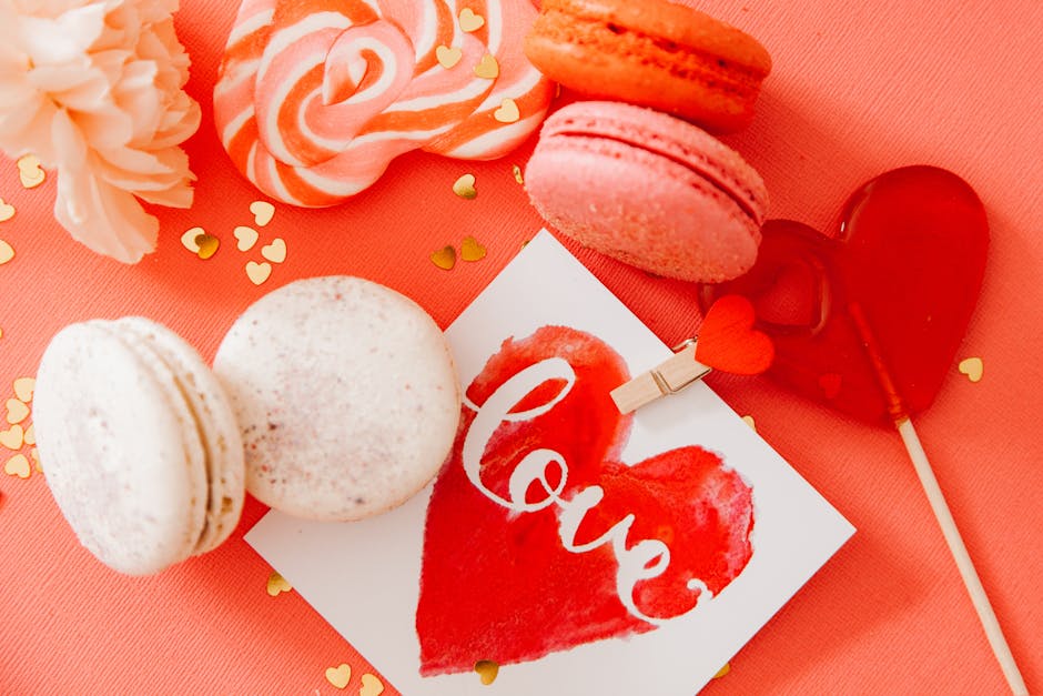 Top view of assorted sweets and a love card on a pink background, perfect for Valentine's Day.