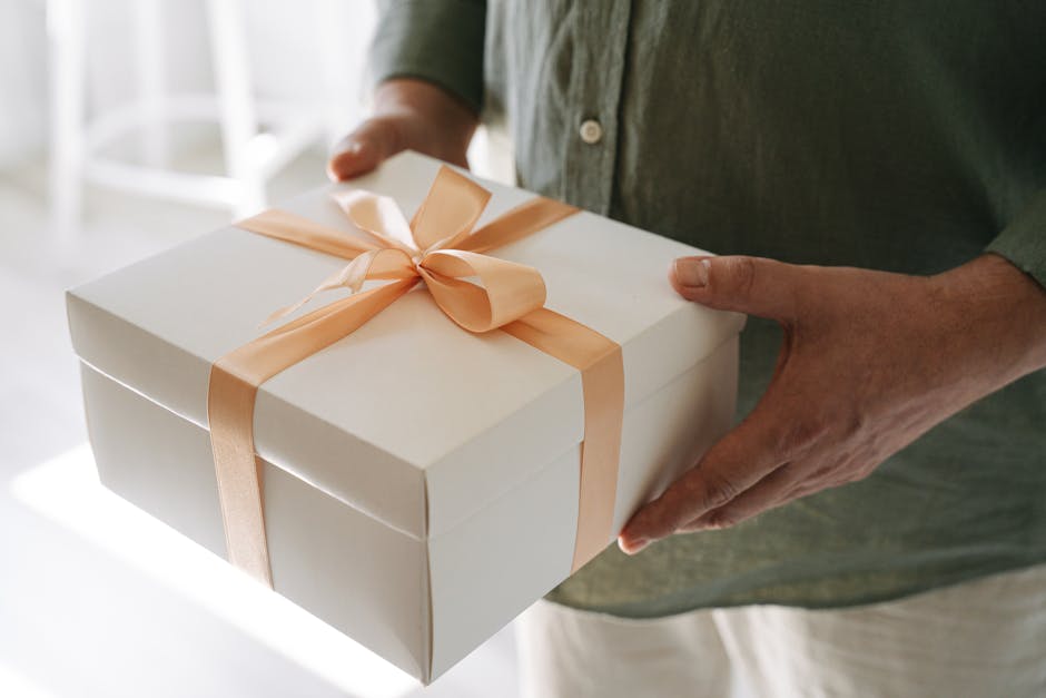 A person holding a white gift box tied with a peach ribbon, symbolizing celebration and surprise.