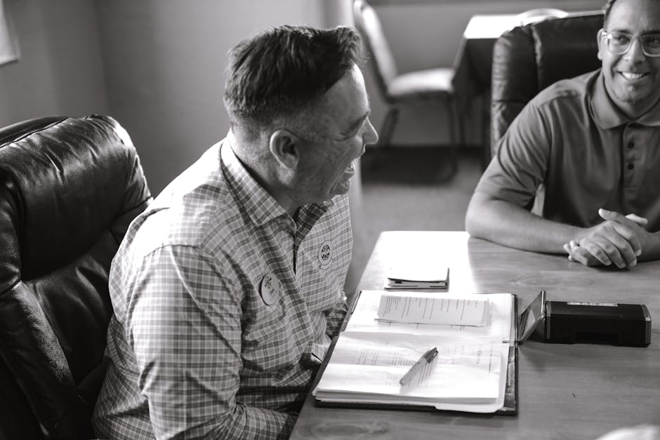 Two men in a business meeting, smiling and laughing, create a light-hearted office atmosphere.