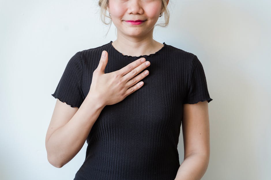 Asian woman in a black shirt expressing gratitude with a hand gesture against a neutral background.