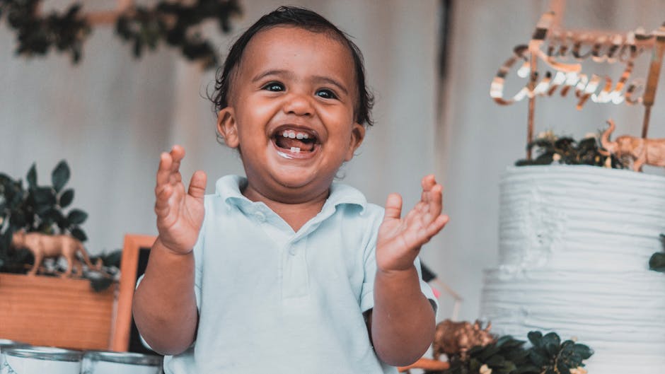 A cheerful child clapping hands excitedly beside a decorated cake at a celebration.