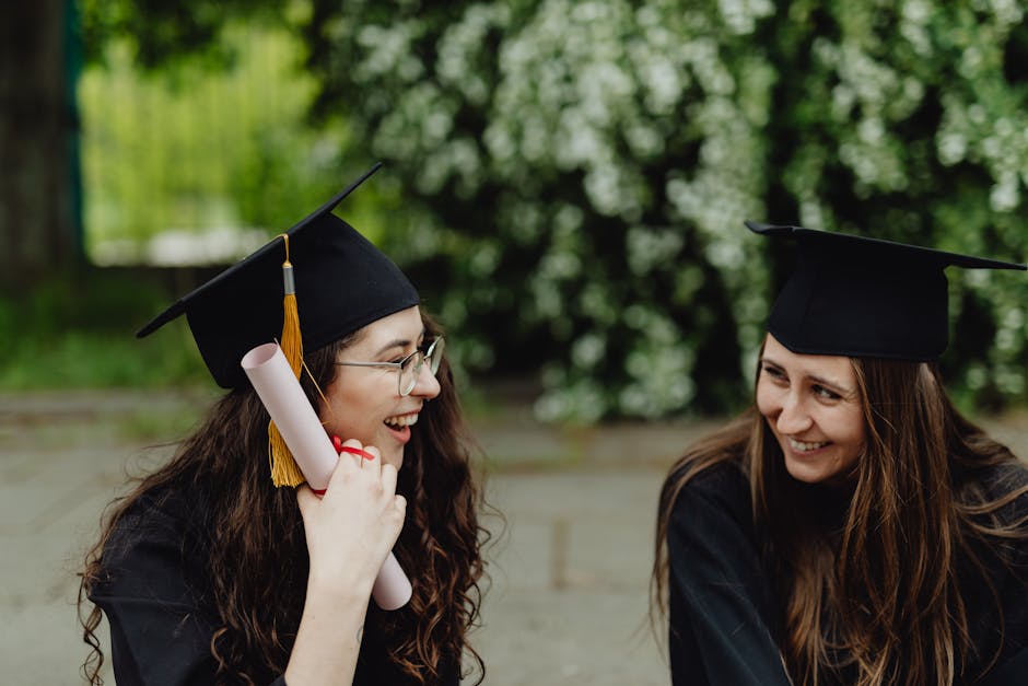 Two women celebrating their graduation with diplomas and caps outdoors.