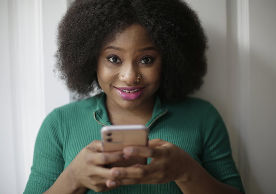 A cheerful woman with afro hair using a smartphone indoors.