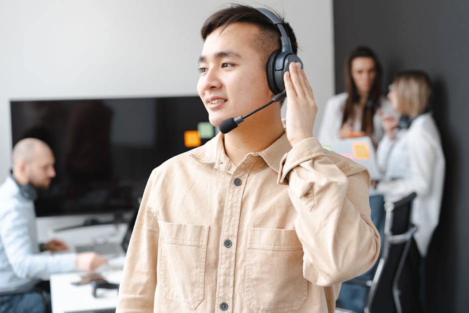 Asian man in beige shirt smiling with headset in modern office setting.