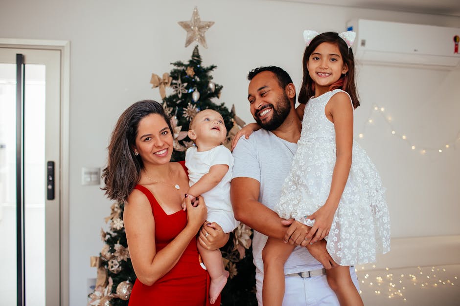 Family of four posing joyfully by a beautifully decorated Christmas tree indoors.