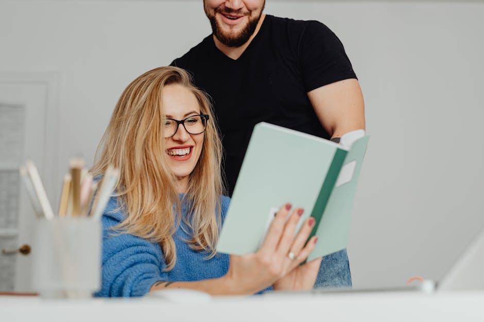 Two office colleagues happily reviewing a notebook, fostering a joyful and productive work atmosphere.