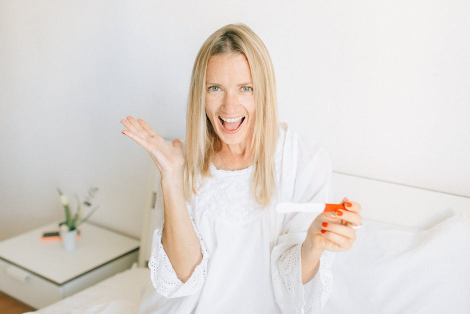 A joyful woman celebrates a positive pregnancy test while sitting on her bed.