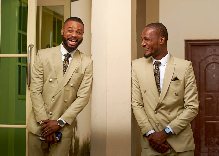 Two African men in suits share a joyful moment at a Nigerian wedding.