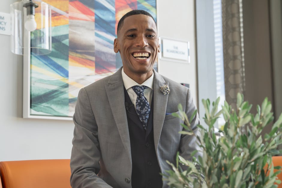 Confident man in a grey business suit smiling warmly in a modern office setting.