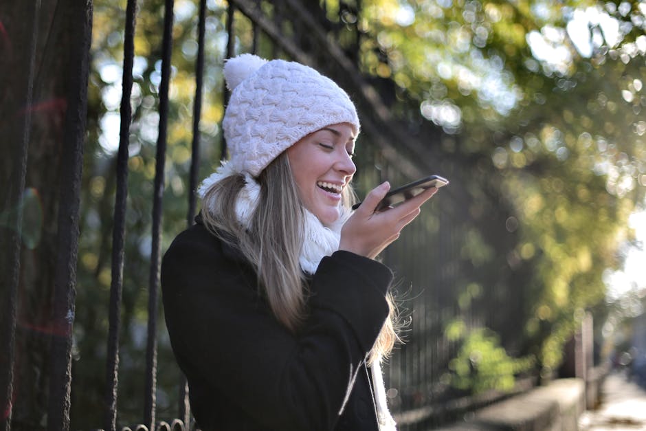 Happy woman in winter attire using smartphone outdoors, enjoying sunny day.