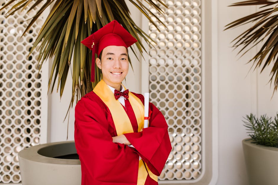 Young graduate in a red cap and gown smiling with diploma outdoors.