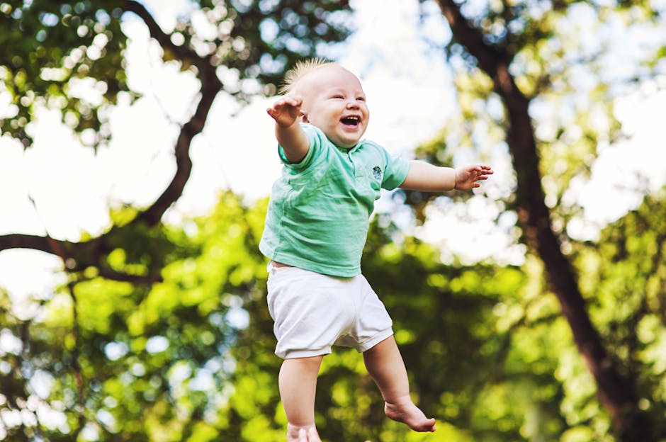 Happy baby wearing a green shirt being tossed in the air on a sunny day in the park.